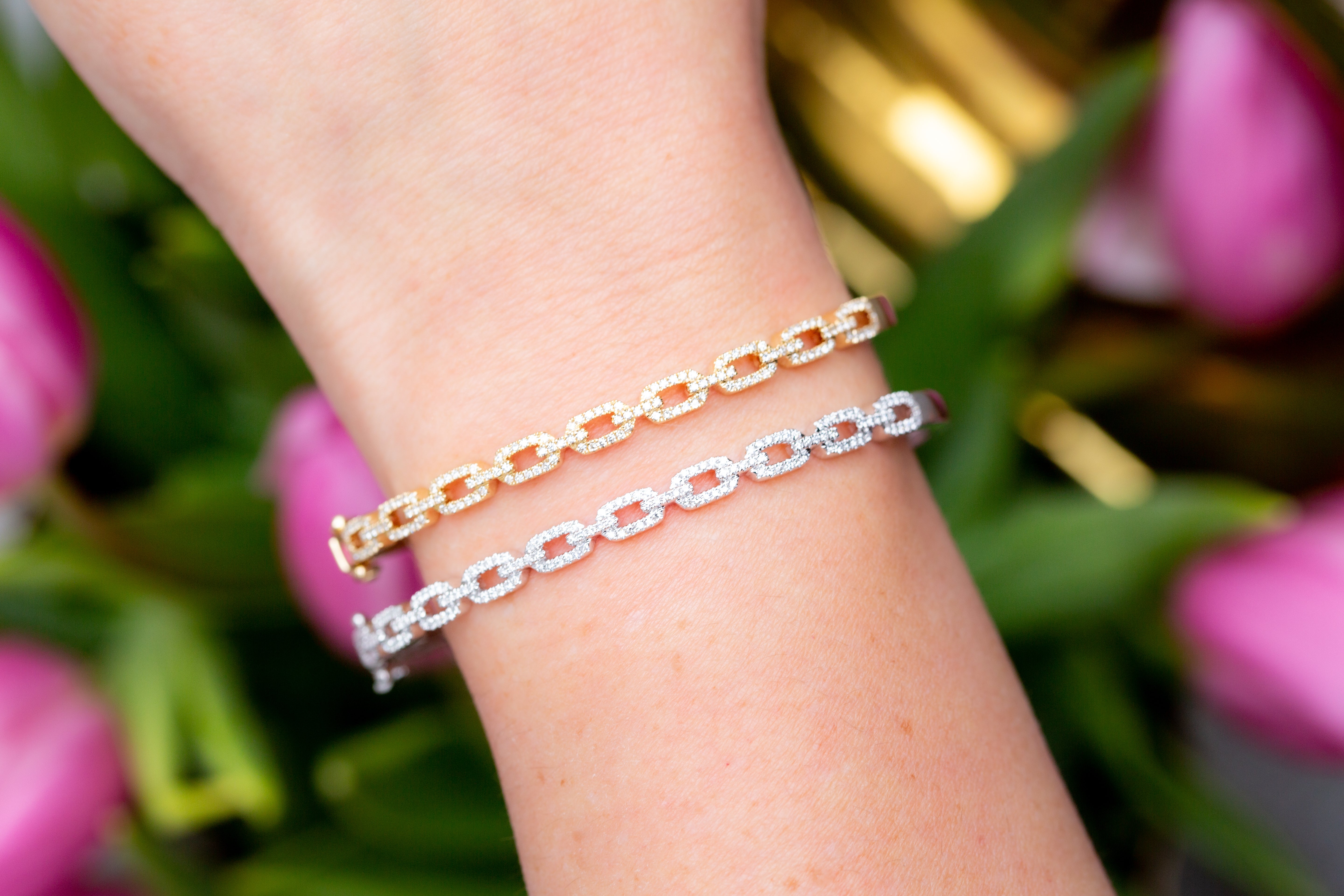 Two chain bracelets on a wrist with pink tulips in the background