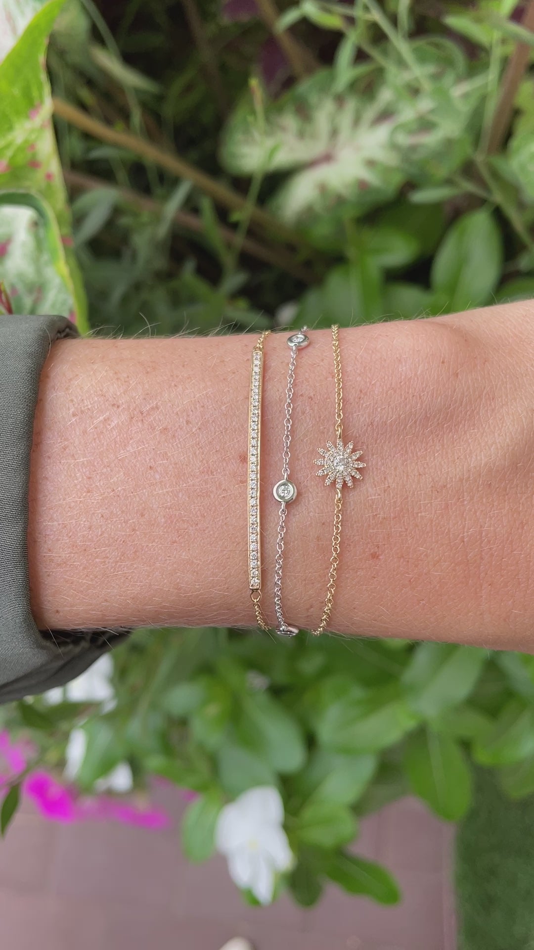 video close-up of three chain bracelets on wrist against green floral background