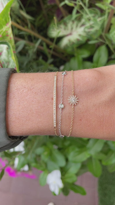 video close-up of three chain bracelets on wrist against green floral background