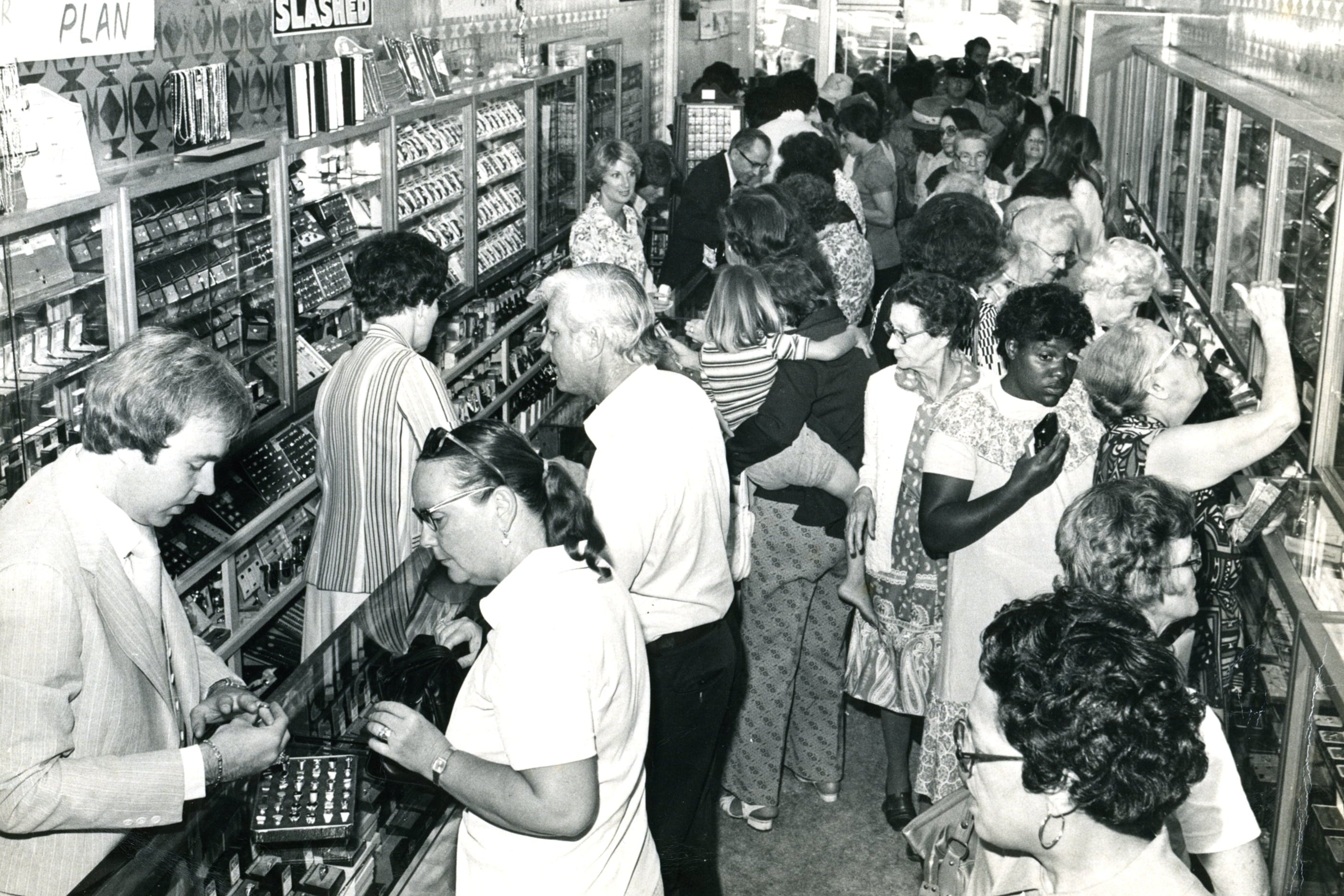 Black and white photograph of a crowded store interior with people shopping.