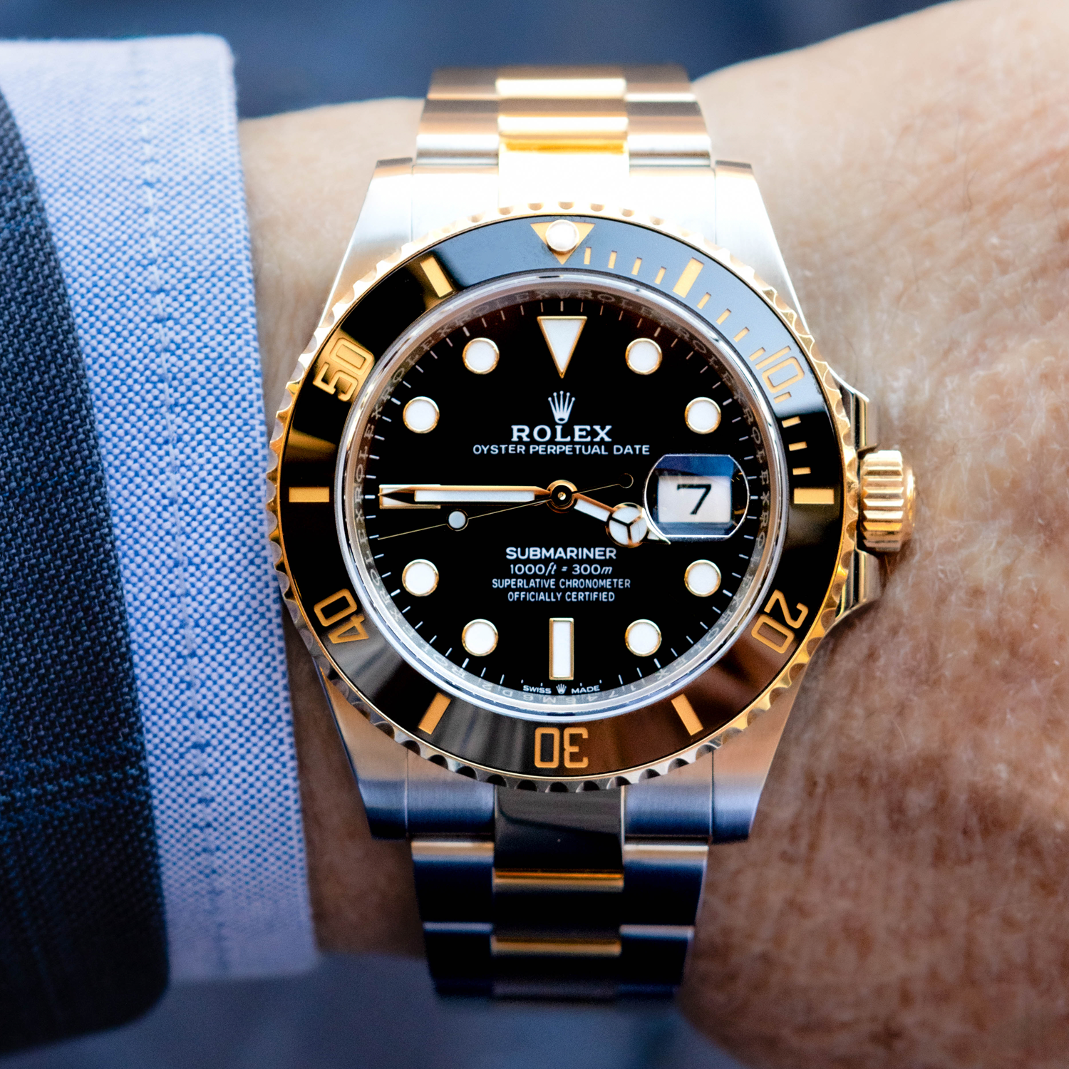 Luxury watch with black dial and gold accents on a wrist against a blue fabric background