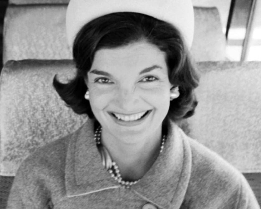 Black and white photo of a woman wearing a coat and hat, sitting on an airplane.