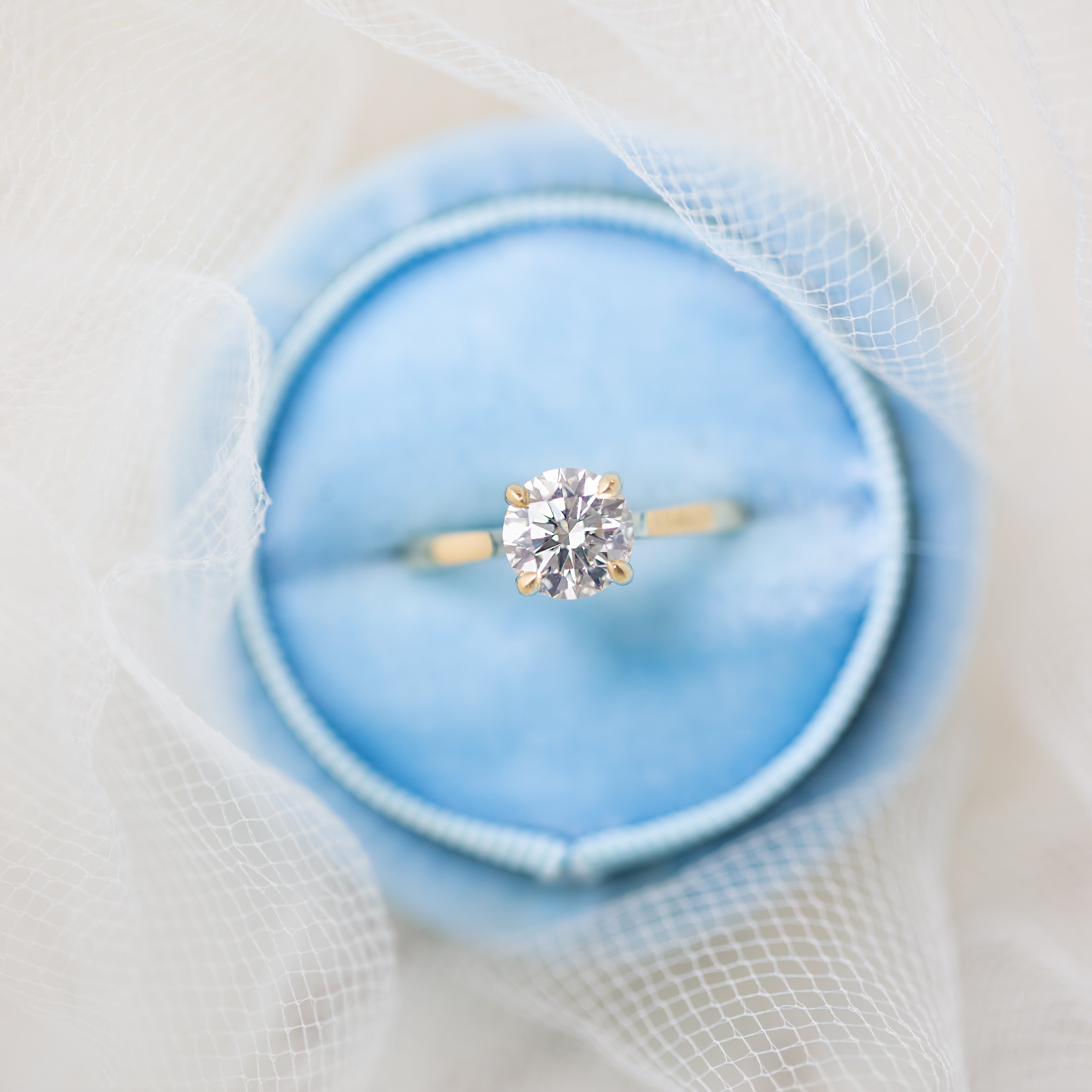 Gold ring with a diamond in a blue jewelry box on a white background